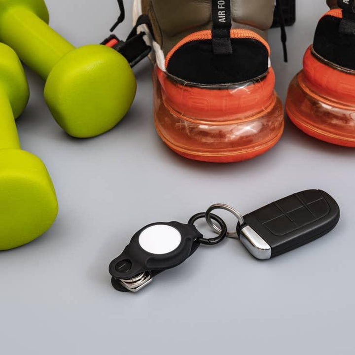 Grüne Hanteln, Sportschuhe mit oranger Sohle und Schlüsselanhänger auf grauem Hintergrund