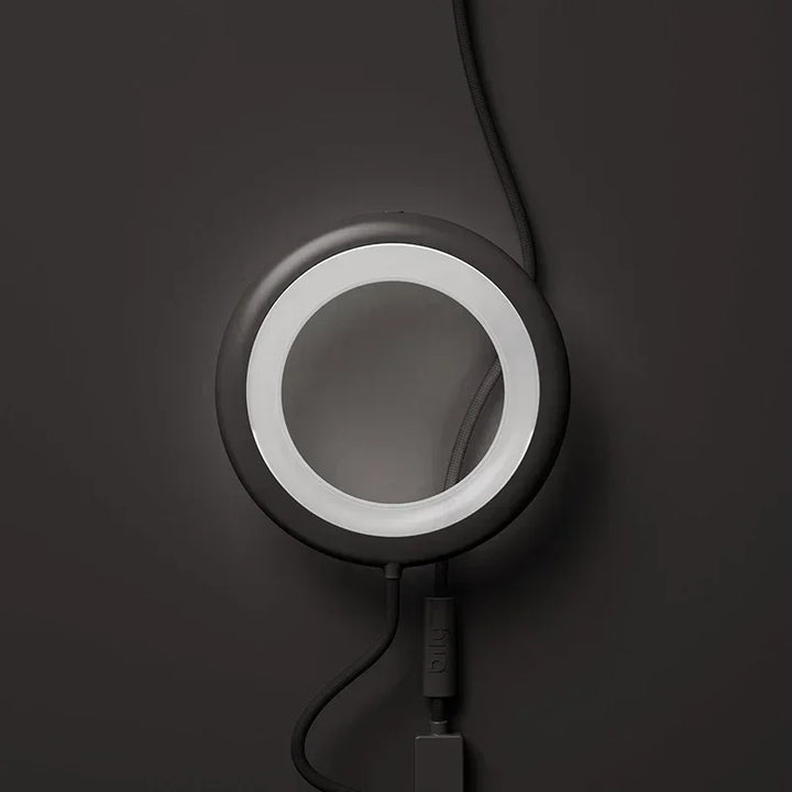 Runde schwarze Tischlampe mit USB-Kabel auf dunklem Hintergrund, modernes Lampendesign