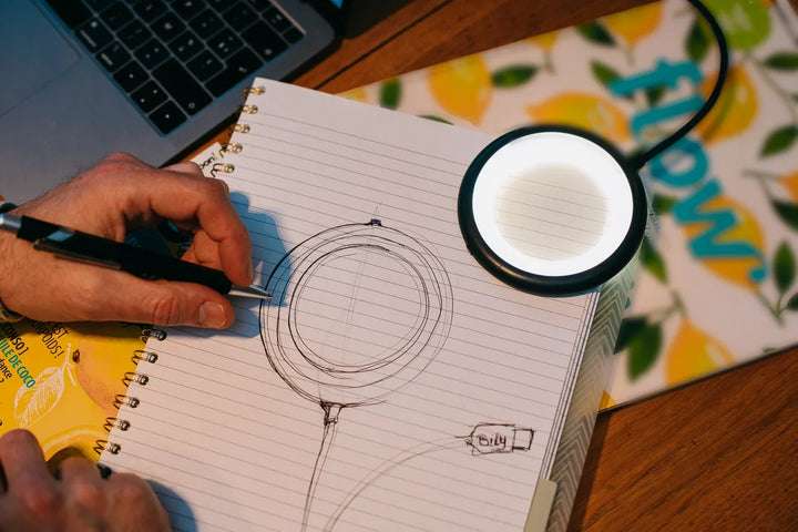 Schwarze Billy Lampe leuchtet Notizbuch mit Skizze auf Schreibtisch neben Laptop