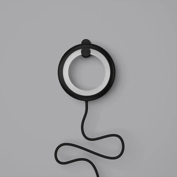 Schwarze runde tragbare Lampe mit Kabel auf grauem Hintergrund, modernes Design.