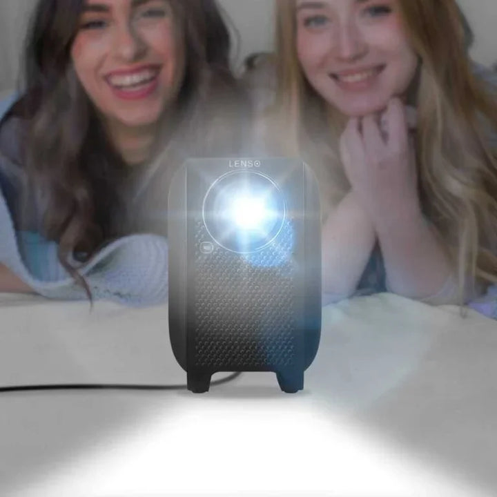 Lenso Mini Beamer projiziert helles Licht, zwei Frauen liegen dahinter auf einem Sofa