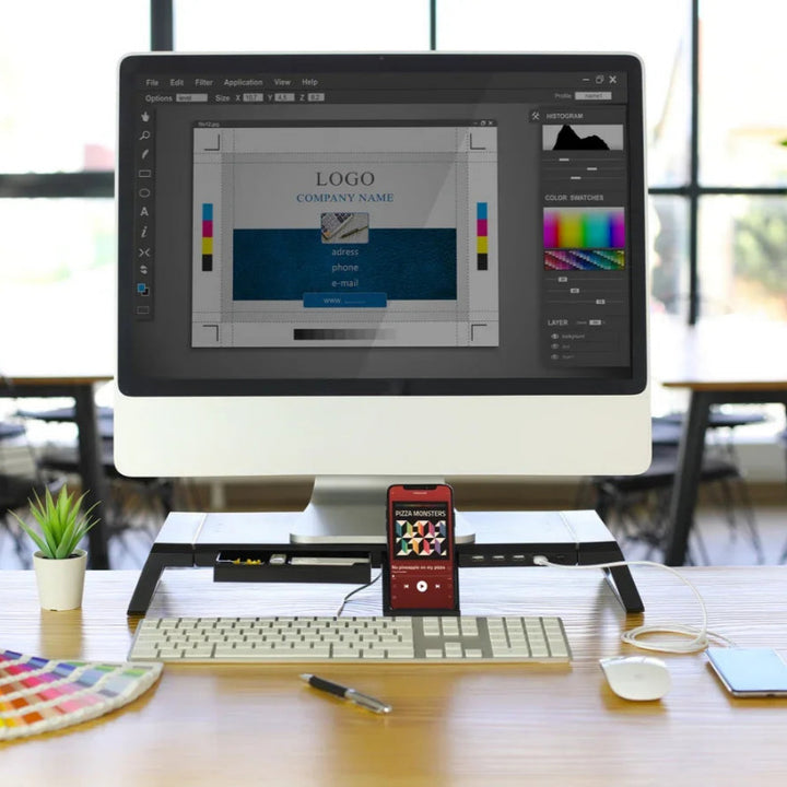 Ein moderner Arbeitsplatz mit einem Computer, auf dem eine Logodesign-Software läuft, einem Smartphone, Farbmustern und einer Schreibtischpflanze.
