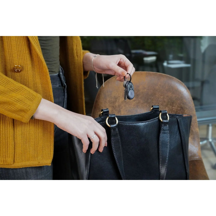 Frau mit Schlüsselbund und Rolling Square Gadget neben schwarzer Handtasche am Stuhl