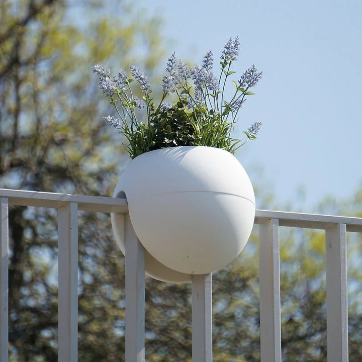 Ein weißer Blumentopf auf einem Geländer, gefüllt mit leuchtend violetten Blumen, bietet ein wunderschönes Arrangement für draußen.