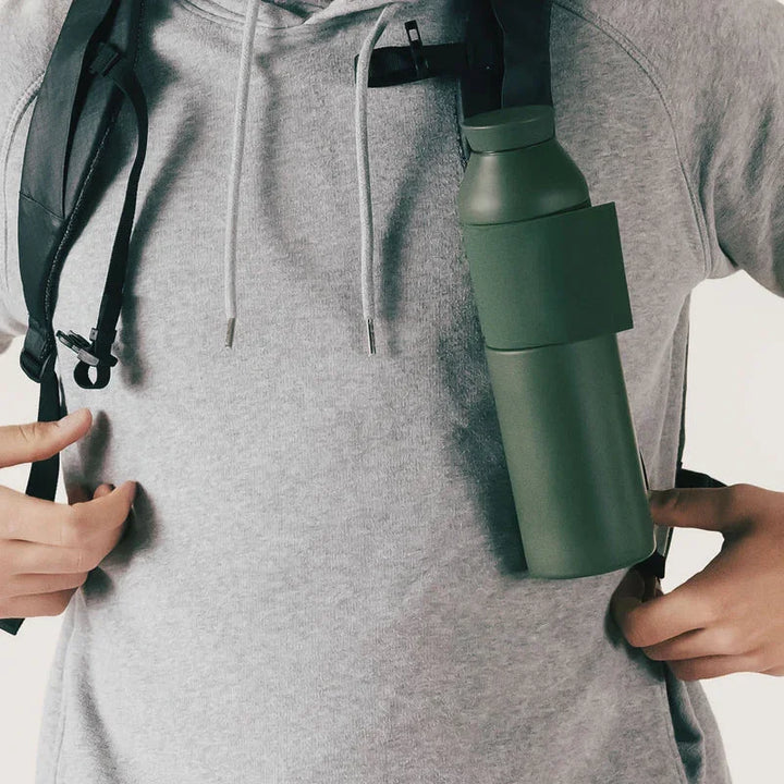 Grüne Closca Trinkflasche aus Edelstahl am Rucksackgurt, Person mit grauem Hoodie