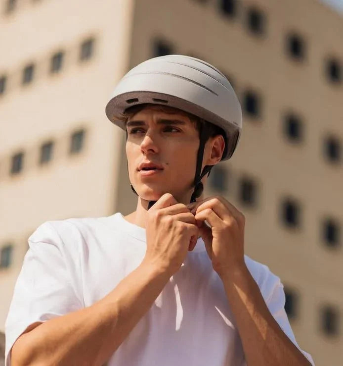 Junger Mann mit urbanem Fahrradhelm vor modernem Gebäude, weißes T-Shirt, sonnige Stadt