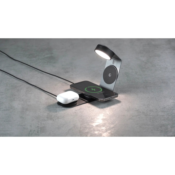 Drahtlose Ladestation mit Lampe lädt Smartphone und kabellose Kopfhörer auf grauem Tisch.