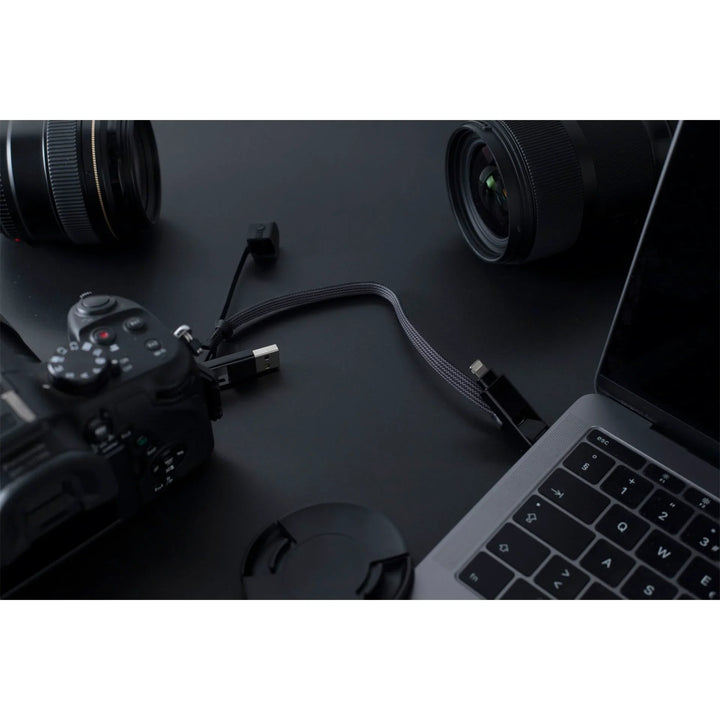 inCharge XL Kabel verbindet Kamera mit Laptop auf schwarzem Tisch, Objektive im Hintergrund
