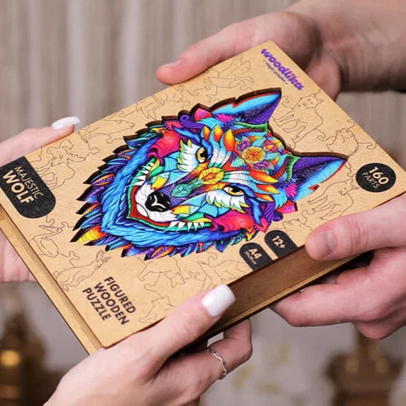 Zwei Hände halten eine bunte Puzzlebox aus Holz mit einer lebendigen Wolfsillustration und der Aufschrift „Majestätischer Wolf, 160 Teile“.