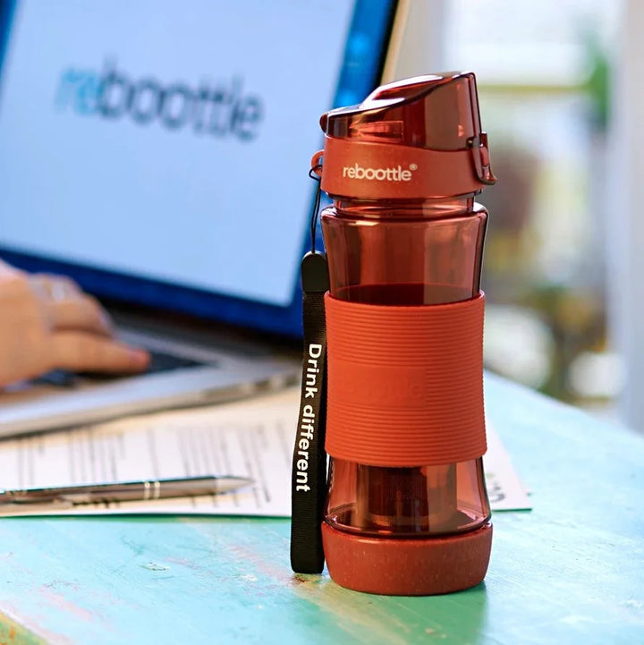 Rote Reboottle Trinkflasche mit Schriftzug auf Holztisch vor Laptop, nachhaltige Wasserflasche