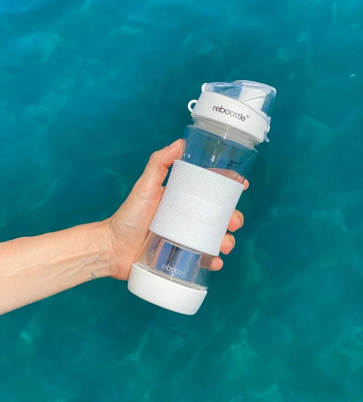 Hand hält transparente Wasserflasche von rebottle mit weißem Deckel vor blauem Wasser