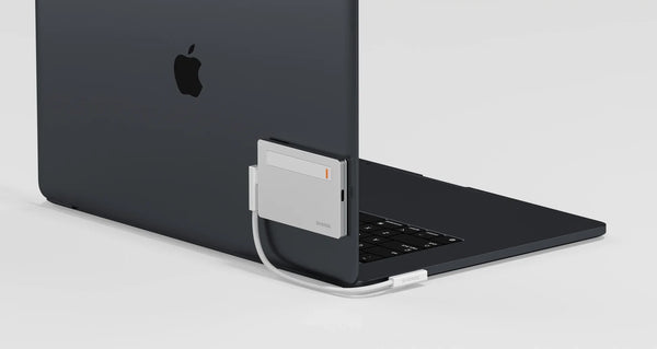 Eine elegante silberne Powerbank, die an der Rückseite eines schwarzen Laptops angebracht ist, wobei das Ladekabel zum USB-C-Anschluss des Laptops führt.