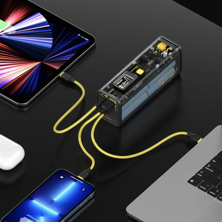 Shargeek 100 Powerbank lädt Tablet, Smartphone und Laptop mit gelben Kabeln am Schreibtisch