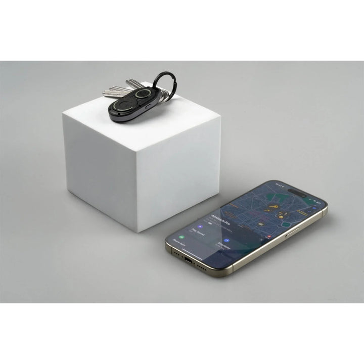 AirNotch Schlüsseltracker mit Schlüsseln auf weißem Würfel neben Smartphone mit Tracking-App