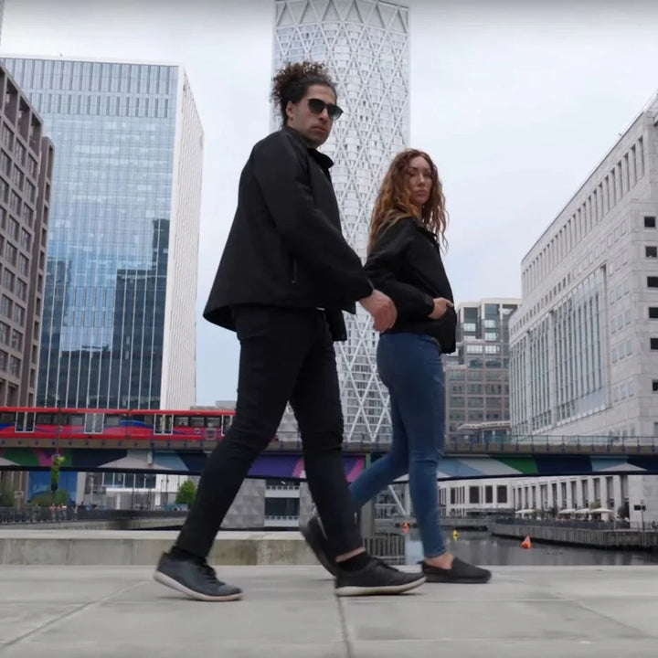 Zwei Personen tragen schwarze Tech-Jacken in urbaner Umgebung mit modernen Hochhäusern.