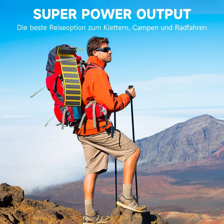 Ein Mann mit einem Rucksack steht auf einem Berg, umgeben von Natur. Auf dem Rucksack ist ein Solarpanel entfaltet.